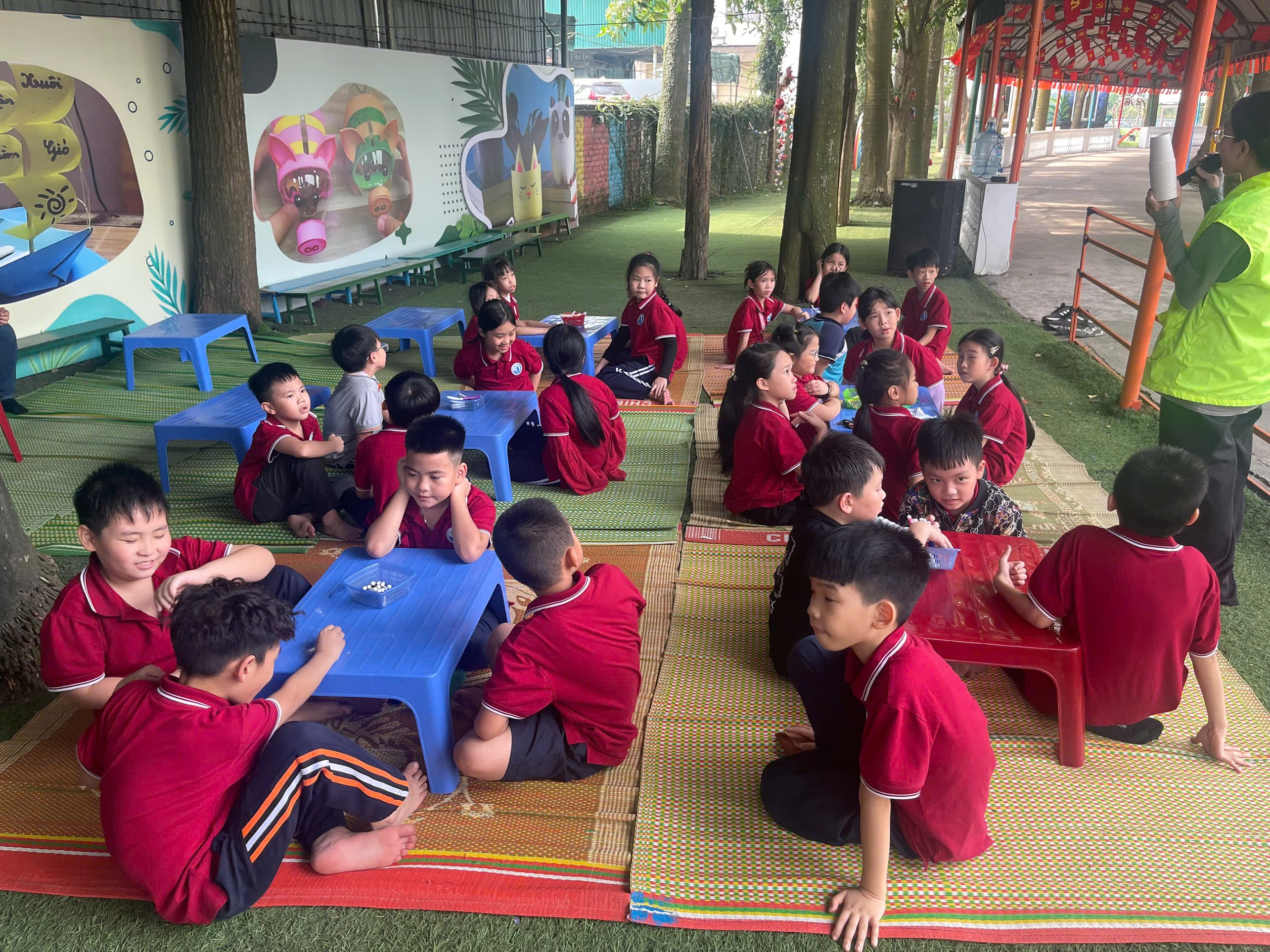 A group of children sitting on a rug outside

Description automatically generated